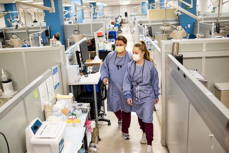 Two dental hygiene students walk through the UMKC dental clinic wearing blue scrubs