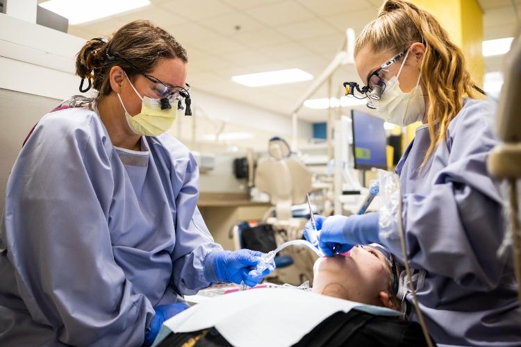 Two dental hygiene students clean a person's teeth in the UMKC dental clinic